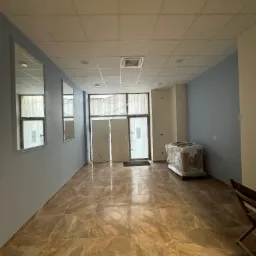 Wnętrze biura z pomalowanymi na niebiesko ścianami, marmurową podłogą, lustrami na ścianie i zapakowanym sprzętem w folii na środku pomieszczenia.