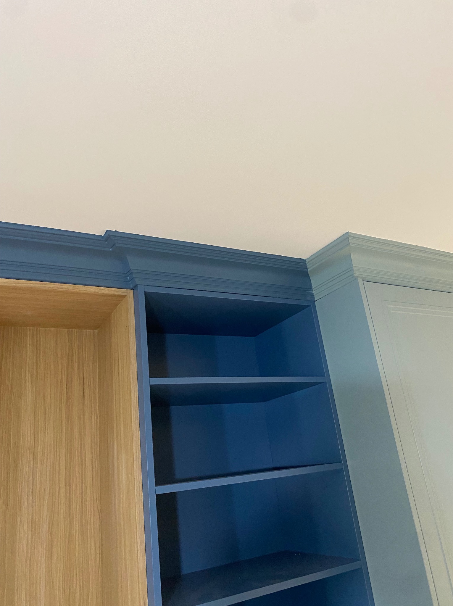 Fragment zabudowy meblowej pod sufitem, z widocznymi półkami w odcieniach niebieskiego i elementami z jasnego drewna.