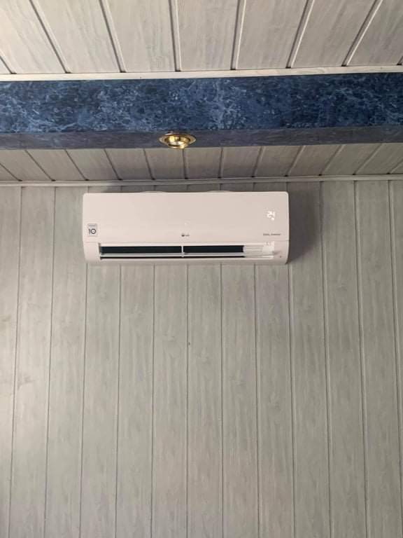 Biała jednostka klimatyzacyjna LG zamontowana na ścianie wyłożonej panelami PCV w kolorze jasnego drewna, pod sufitem z drewnianą belką i punktowym oświetleniem.