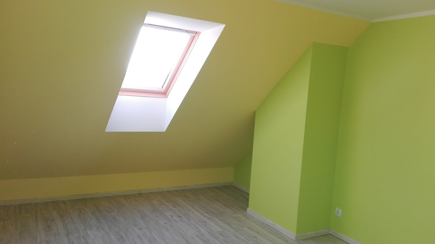 Pomalowane na limonkowo-żółto poddasze ze skośnym dachem i oknem dachowym, widoczna jasnoszara podłoga.