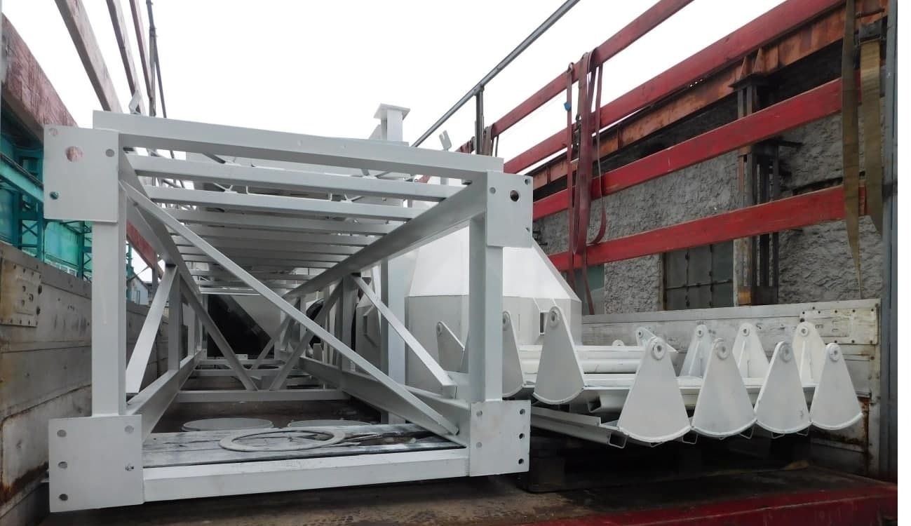 Konstrukcja stalowa pomalowana na biało, przewożona na platformie transportowej z czerwonymi elementami zabezpieczającymi.