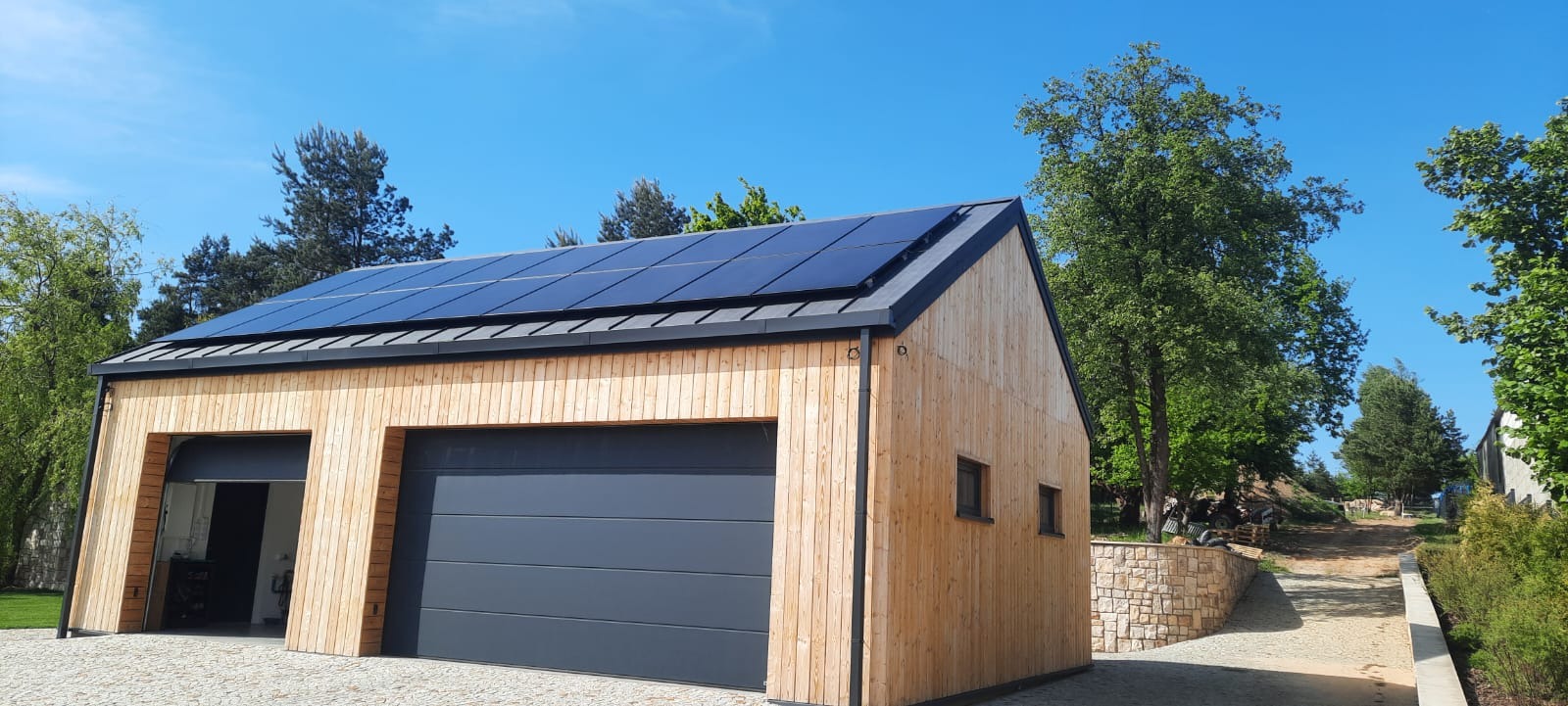 Nowoczesny garaż z drewnianą elewacją i panelami słonecznymi na dachu, jasne niebo w tle.