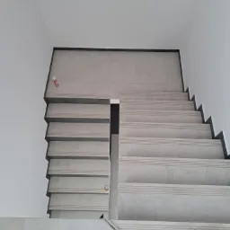 Wykończone schody z szarych płytek z ciemnoszarymi krawędziami, widok z góry, z narzędziami do fugowania na podłodze.