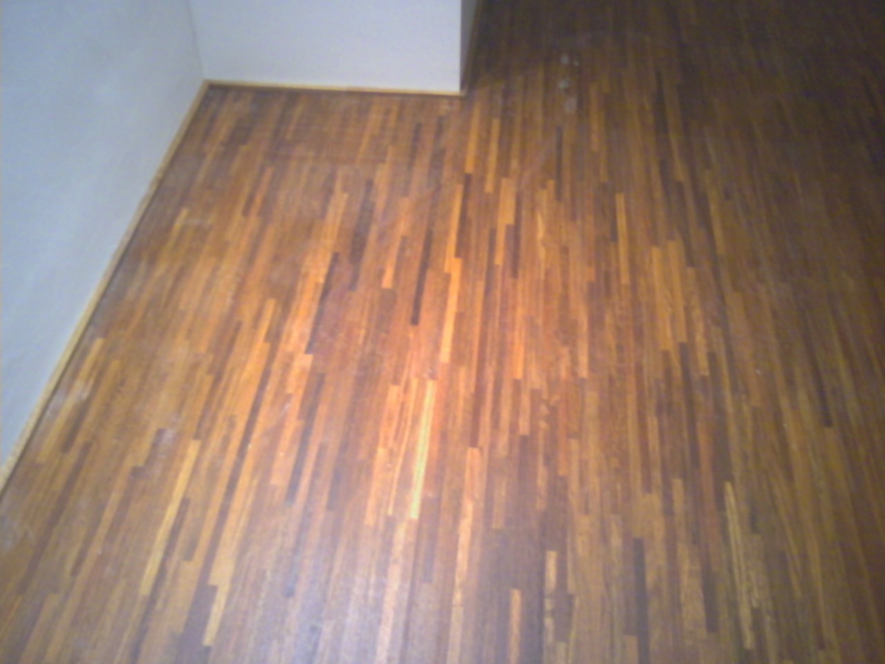 Ułożony parkiet przemysłowy z drewna w odcieniach brązu, widok z góry na fragment podłogi przy ścianie.