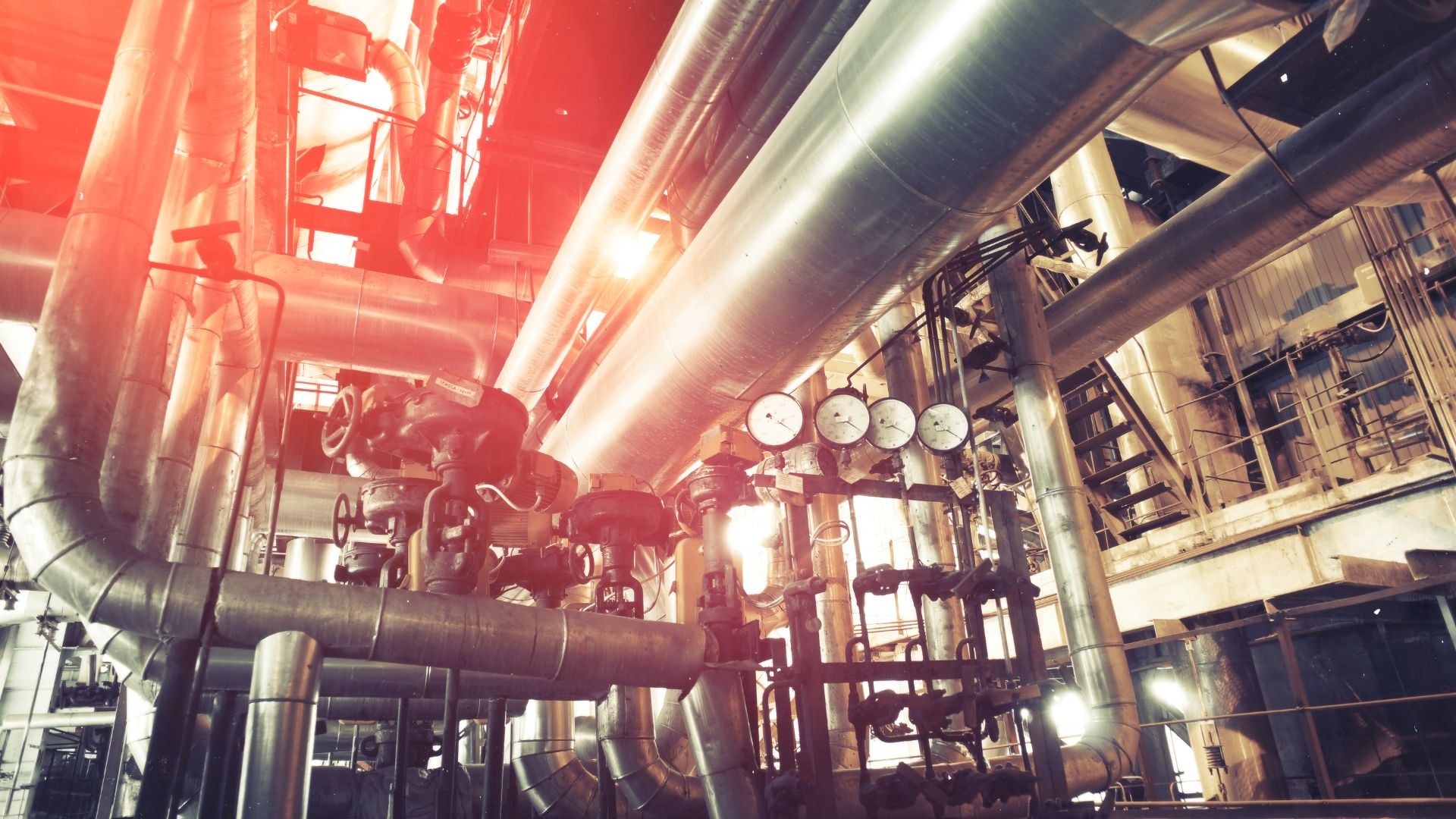 Złożony system rur, zaworów i manometrów w instalacji przemysłowej, oświetlony ciepłym światłem.