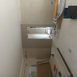 Wnętrze w trakcie remontu: widoczne płyty gipsowo-kartonowe, drabina, materiały izolacyjne i narzędzia, ściany przygotowane do dalszych prac wykończeniowych.