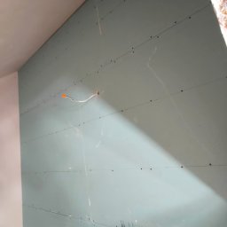 Yuriy Romanenko usługi budowlane - Ściana z zamontowaną płytą gipsowo-kartonową, widoczne ślady szpachlowania i przewód elektryczny wystający ze ściany, przygotowana do dalszych prac wykończeniowych.