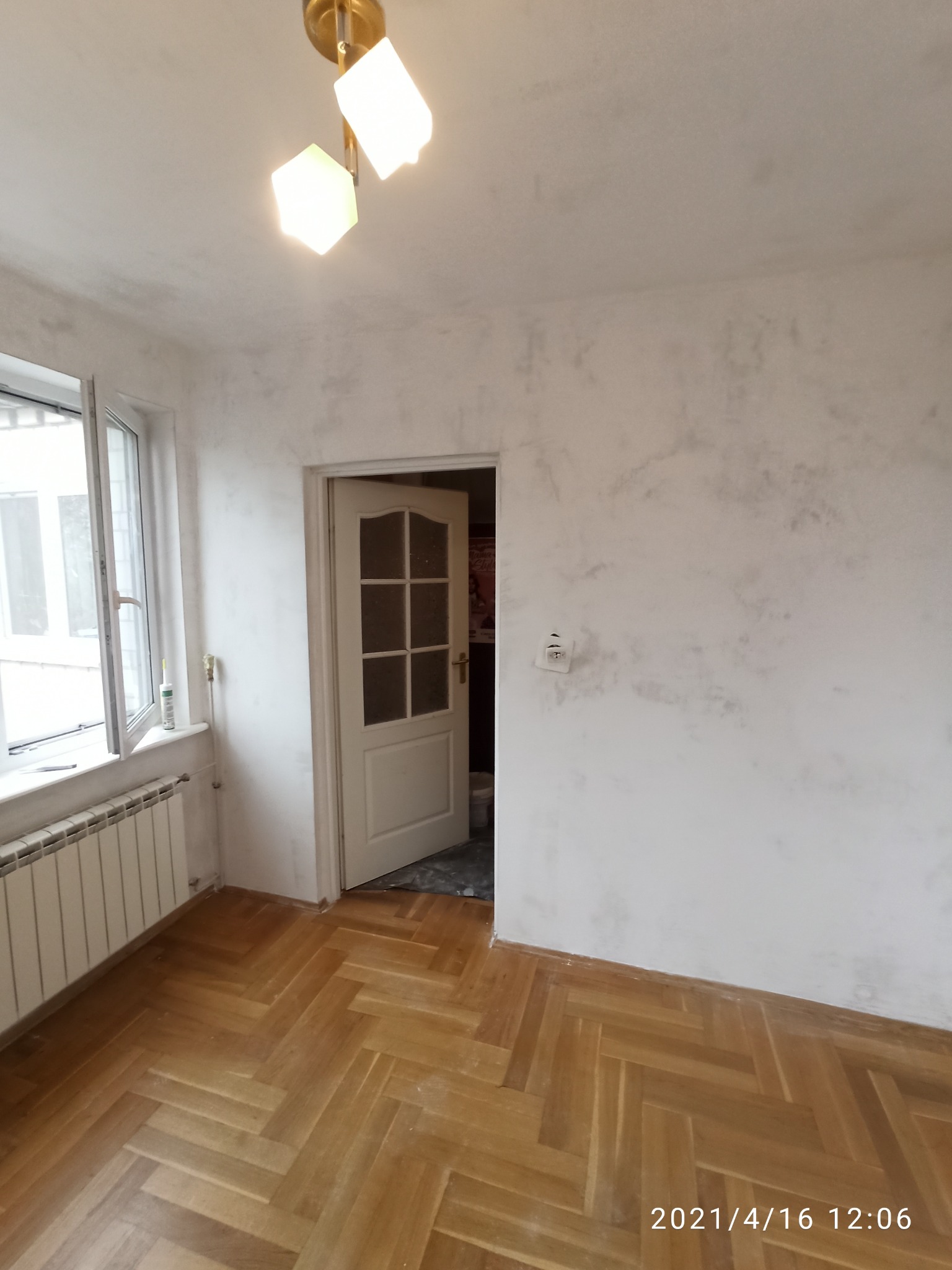 Pokój po remoncie: parkiet ułożony w jodełkę, ściany z efektem dekoracyjnym, białe okno z grzejnikiem i otwarte białe drzwi z przeszkleniami.