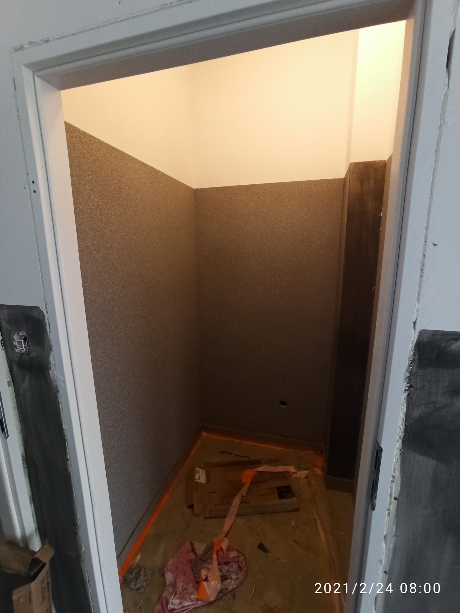 Niewielkie pomieszczenie po remoncie z wykończonymi ścianami w odcieniach brązu, widoczne kartony i ślady po remoncie na podłodze.