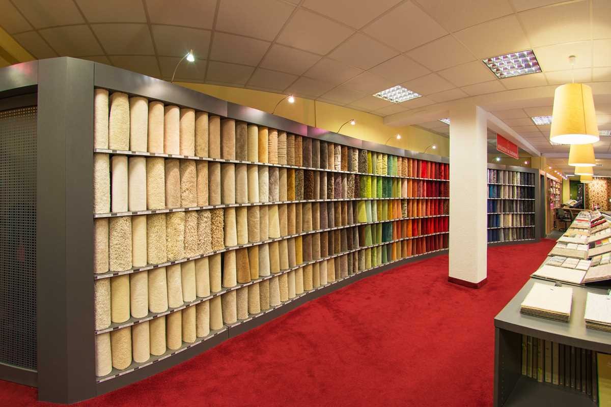 Salon z ekspozycją wykładzin dywanowych w rolkach, ułożonych kolorystycznie, na czerwonej podłodze.