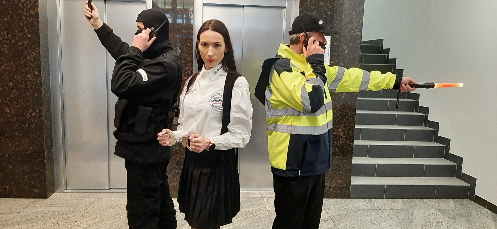 Trzech pracowników ochrony w różnych strojach: mężczyzna w kominiarce z radiem i kamizelką taktyczną, kobieta w białej koszuli z napisem 'SECURITY' i spódniczce trzymająca kajdanki oraz mężczyzna...