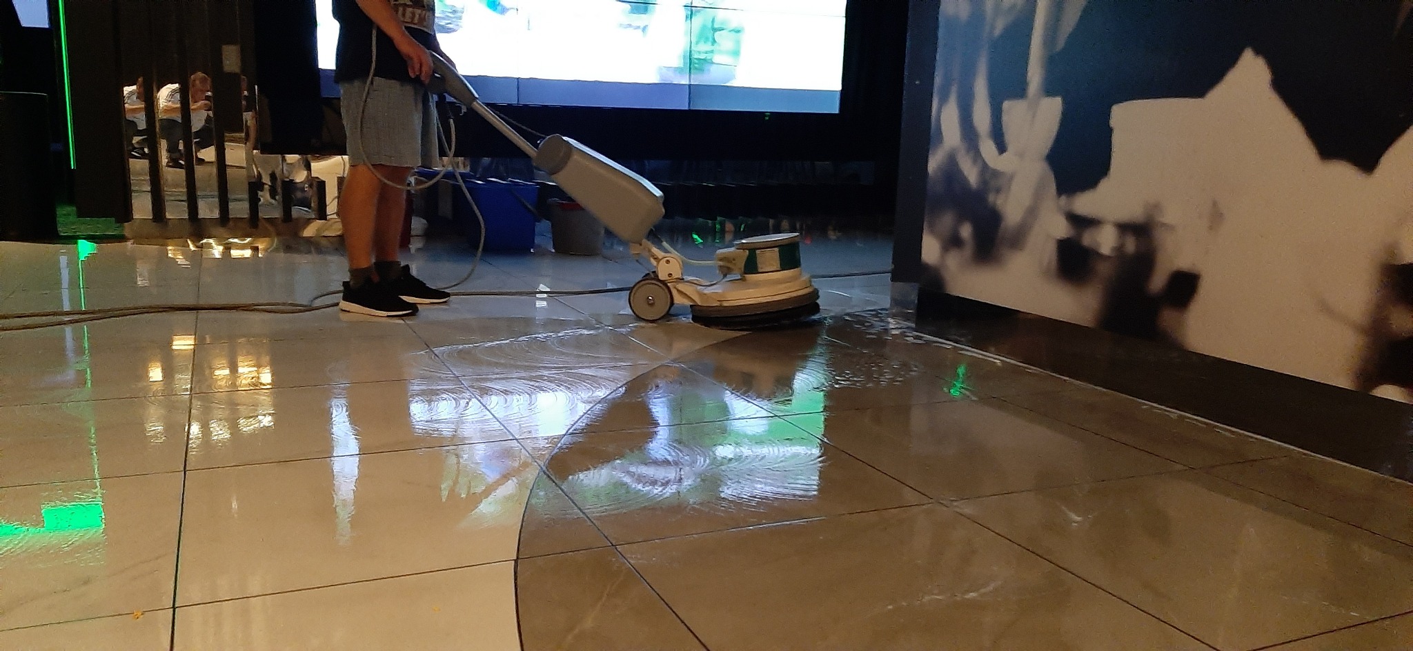 Polerowanie podłogi w lokalu usługowym za pomocą maszyny czyszczącej; widoczne odbicia w wypolerowanej posadzce.
