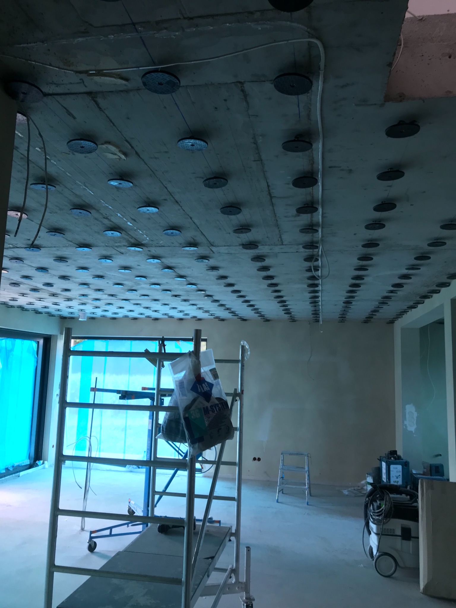 Przygotowanie sufitu do dalszych prac wykończeniowych: widoczne zamocowane uchwyty pod instalacje, rusztowanie, drabina i narzędzia w surowym wnętrzu.