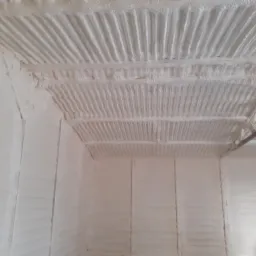 Wnętrze pomieszczenia z widoczną strukturą natryśniętej, jasnej pianki izolacyjnej na ścianach i suficie z blachy trapezowej.