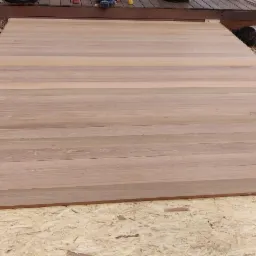 Fragment tarasu z desek kompozytowych w trakcie budowy, widoczne narzędzia i osoba w tle, podłoże z płyty OSB.