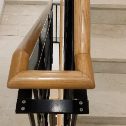 Widok z góry na marmurowe schody z drewnianą poręczą i czarnymi metalowymi wspornikami, z plecakiem leżącym na jednym ze stopni.