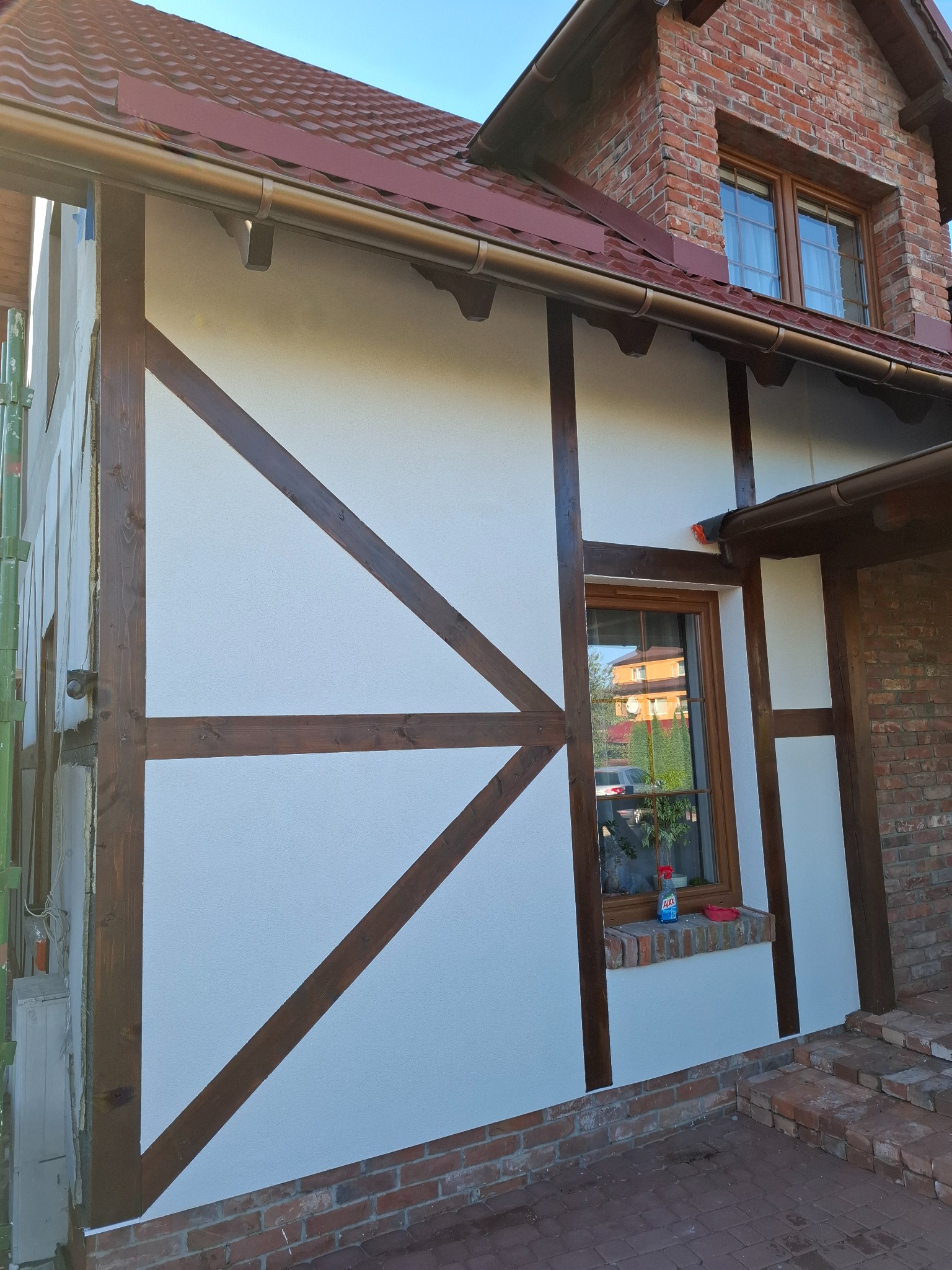 Elewacja domu w stylu muru pruskiego po renowacji, z widocznymi drewnianymi belkami i świeżo otynkowaną białą ścianą. Widoczne detale wykończeniowe i ceglana podmurówka.