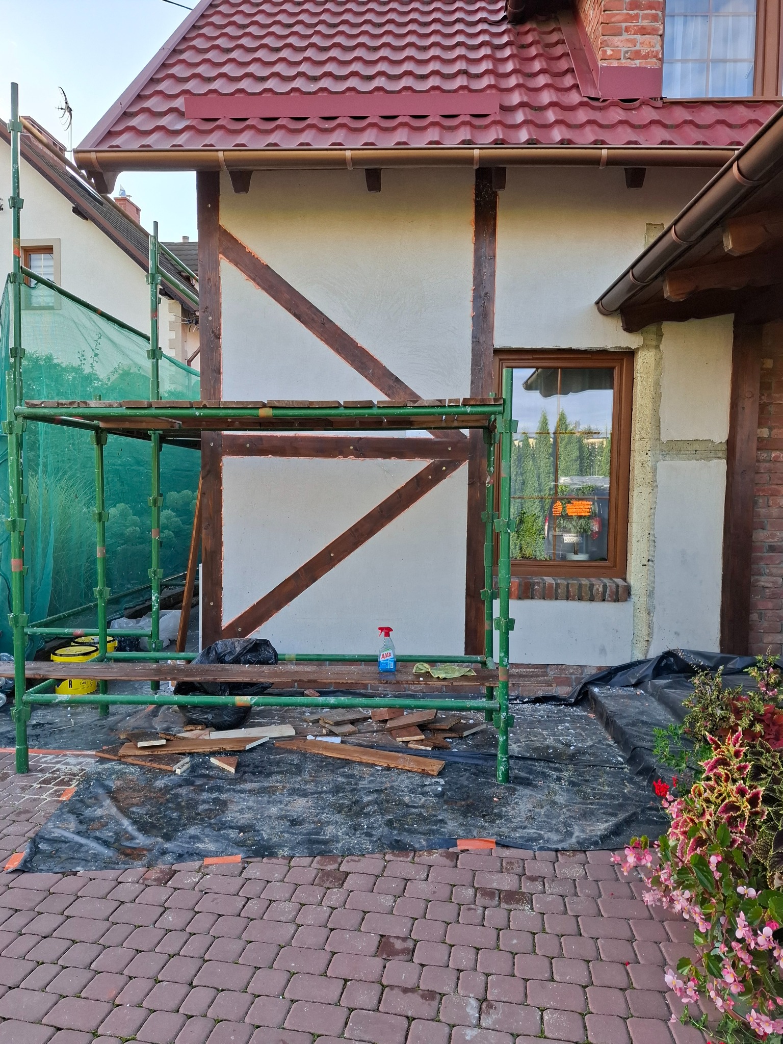 Elewacja domu w trakcie renowacji z widocznymi rusztowaniami, fragmentami ocieplenia i drewnianą konstrukcją szkieletową. Prace w toku, widoczne narzędzia i materiały.
