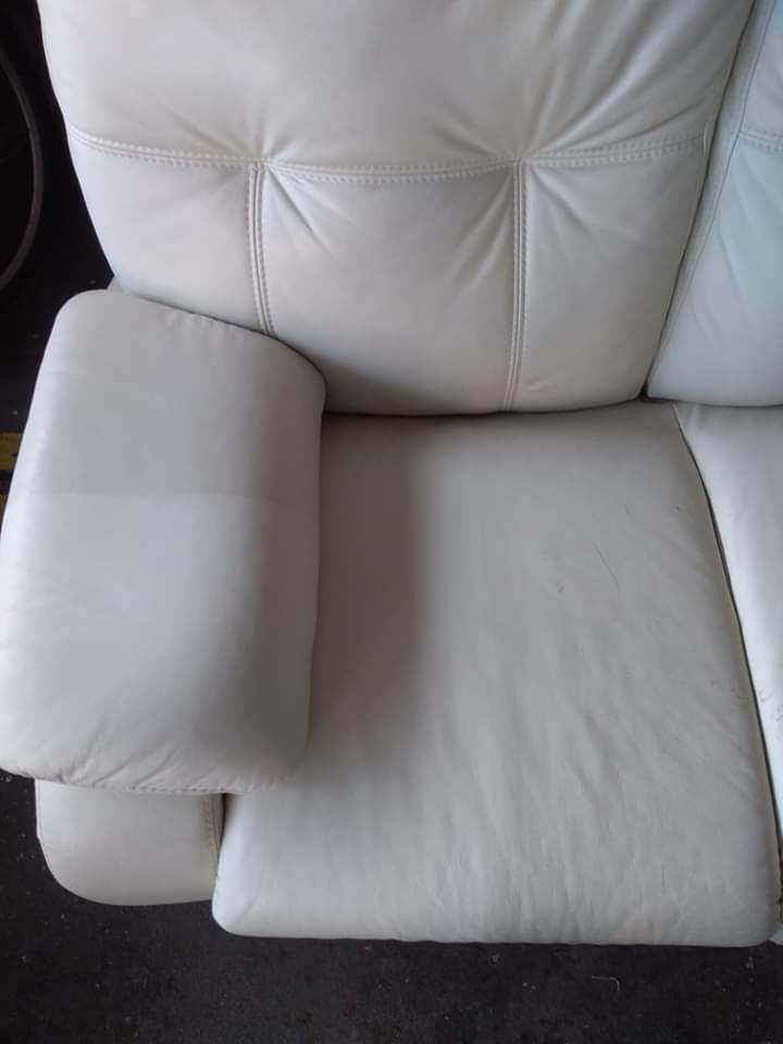 Fragment kremowej, skórzanej kanapy z widocznymi przeszyciami, lekko zabrudzona na siedzisku i podłokietniku.