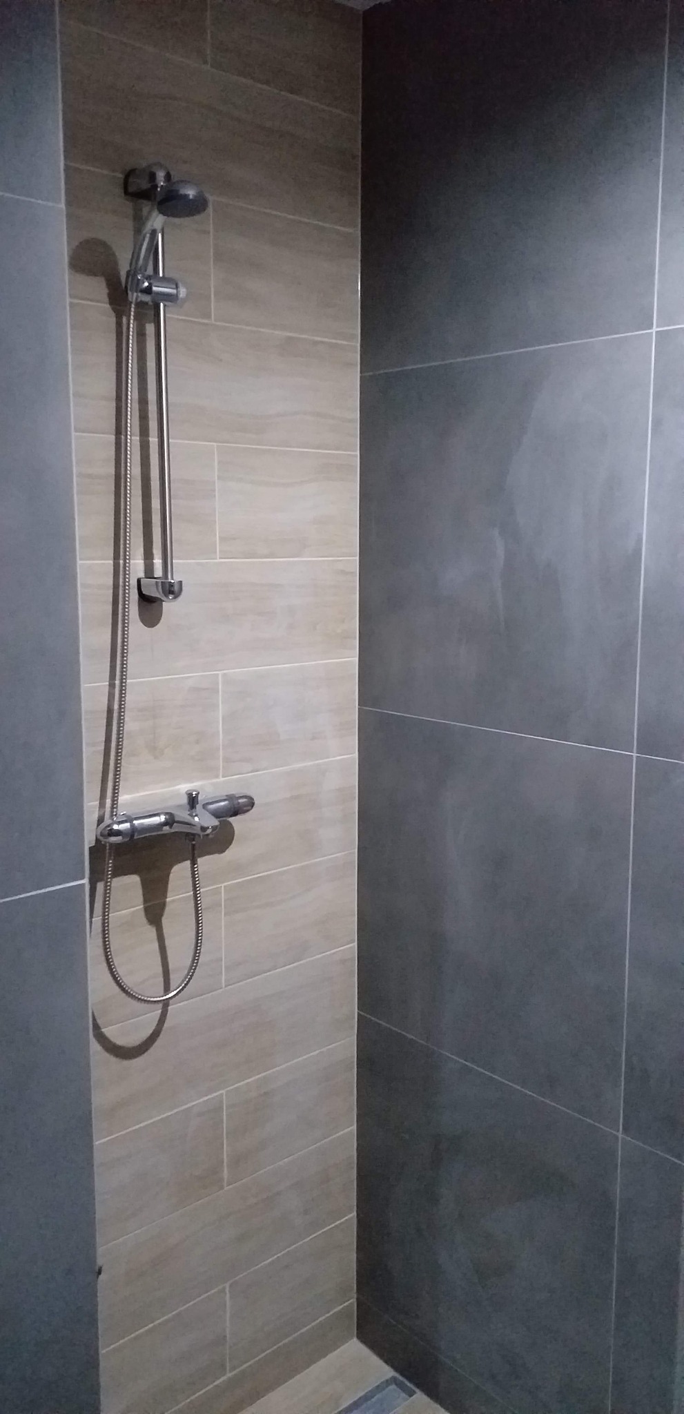 Nowoczesna kabina prysznicowa z chromowaną armaturą i płytkami w odcieniach beżu i szarości, widoczne łączenia płytek.