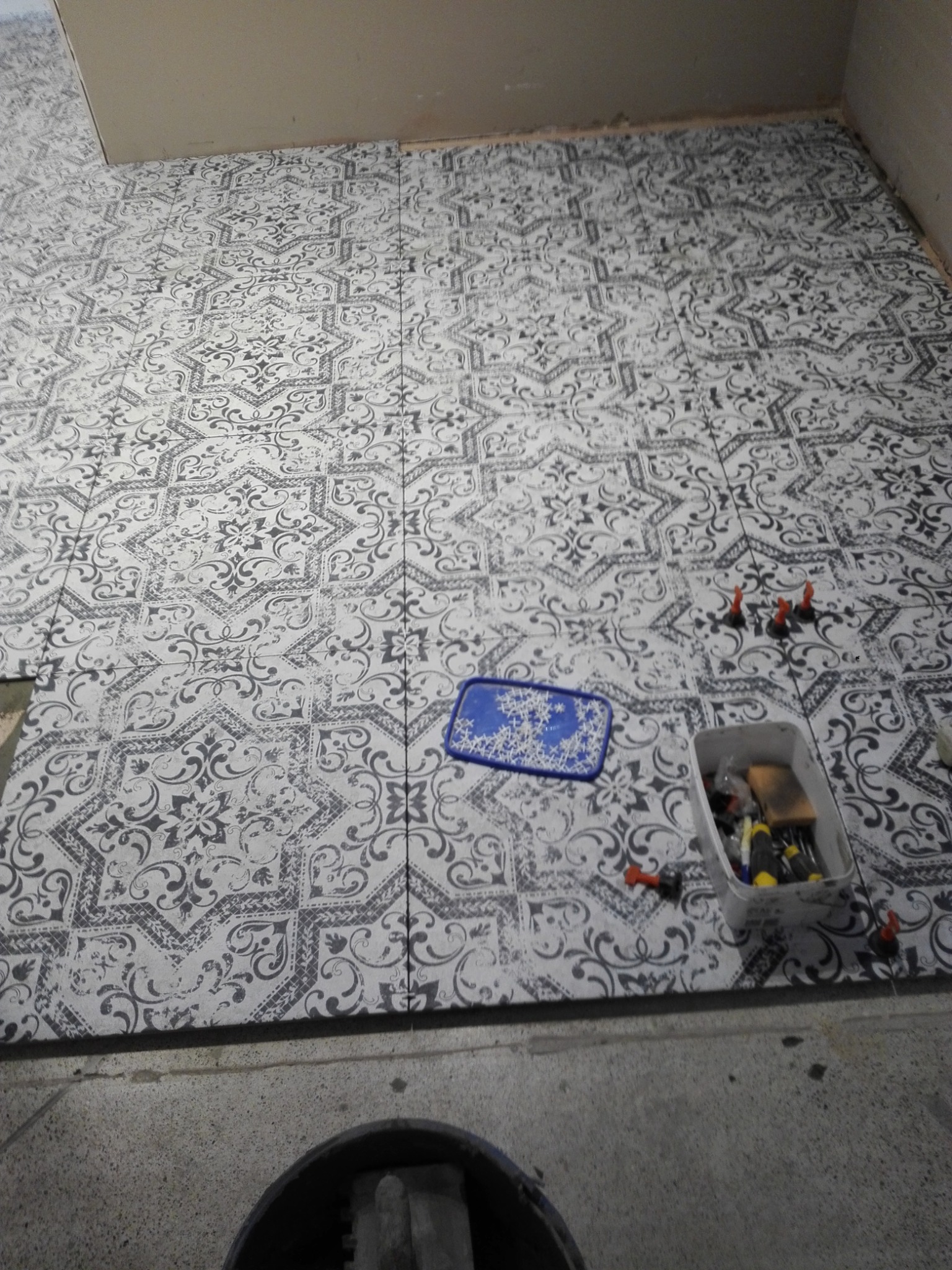 Układanie wzorzystych płytek podłogowych w trakcie prac, widoczne narzędzia, poziomica i krzyżyki dystansowe.