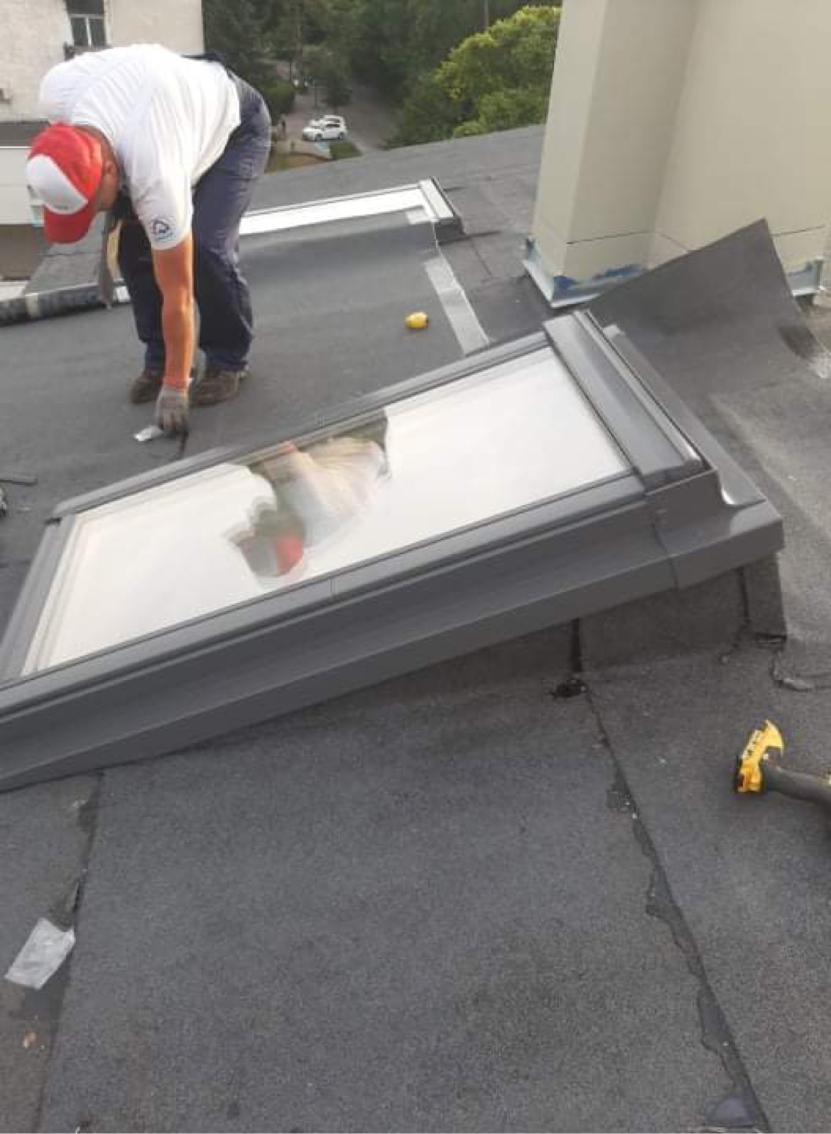 Monter w trakcie montażu okna dachowego na płaskim dachu pokrytym papą, widoczne narzędzia i elementy uszczelniające.