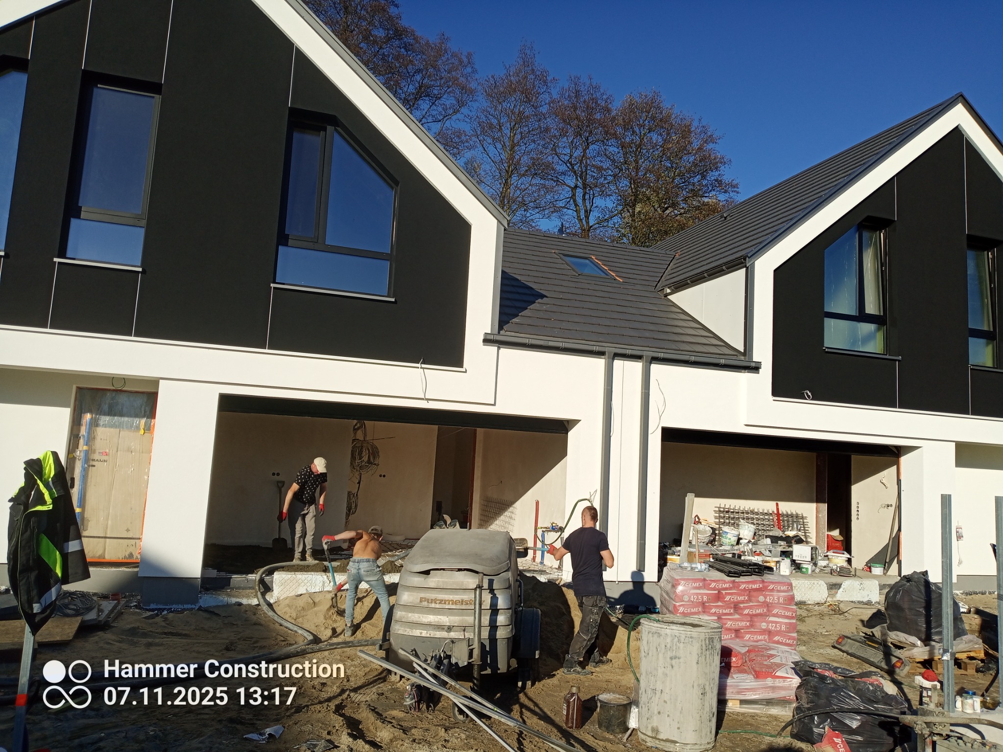 Prace wylewkowe w nowoczesnym domu jednorodzinnym. Ekipa w trakcie pracy z maszyną Putzmeister. Worki z cementem CEMEX. Widoczne elementy konstrukcji budynku.