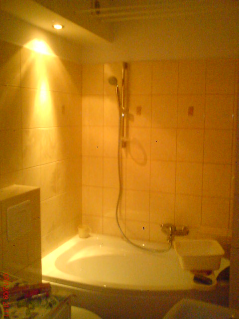 Wykończona łazienka w Strzeszewie z narożną wanną, prysznicem i beżowymi płytkami, oświetlona punktowym światłem.