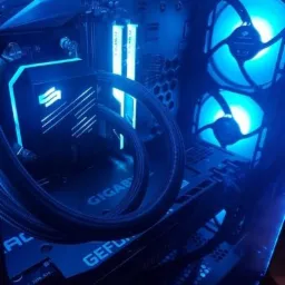 Podświetlony na niebiesko wnętrze komputera stacjonarnego z chłodzeniem wodnym, pamięcią RAM i wentylatorami. Widoczna płyta główna Gigabyte i karta graficzna GeForce.