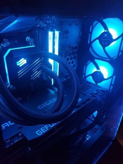 Podświetlony na niebiesko wnętrze komputera stacjonarnego z chłodzeniem wodnym, pamięcią RAM i wentylatorami. Widoczna płyta główna Gigabyte i karta graficzna GeForce.