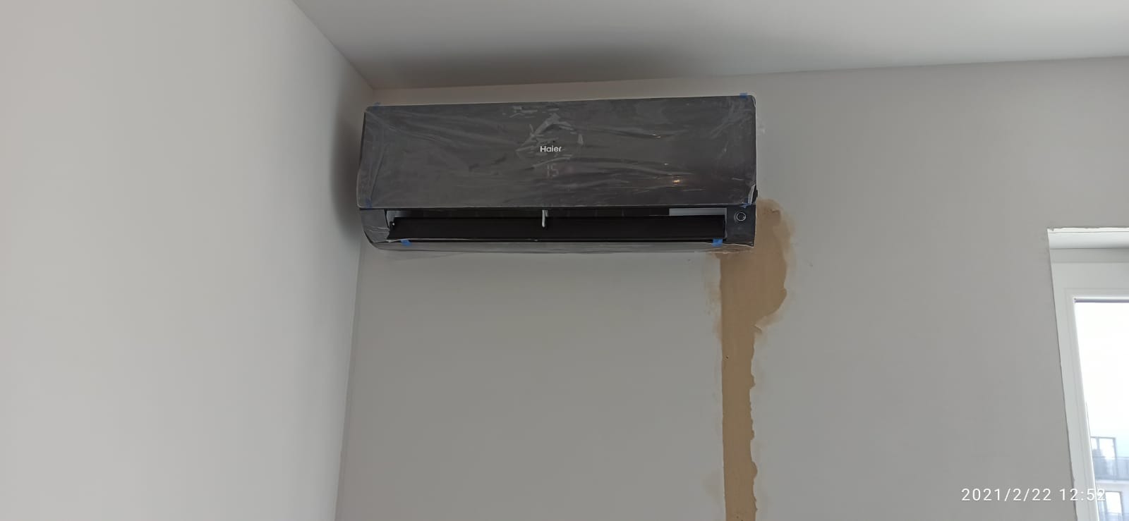 Zamontowany klimatyzator Haier w folii ochronnej na białej ścianie, widoczne ślady po montażu i niedomalowane fragmenty ściany.