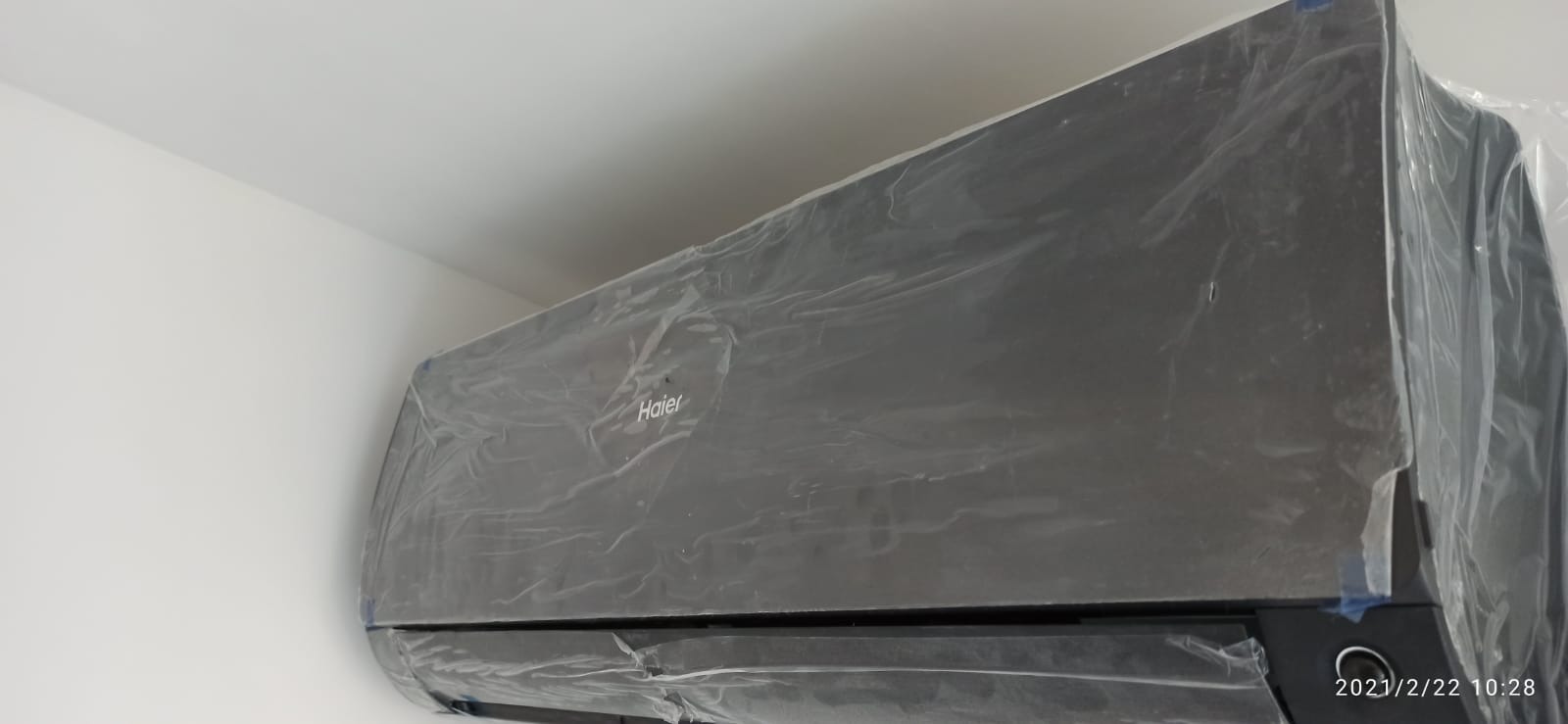 Nowy, czarny klimatyzator marki Haier, zabezpieczony folią ochronną, zamontowany na białej ścianie.