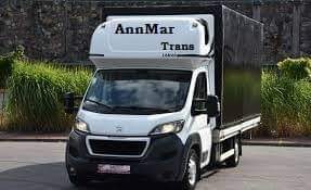 Biały samochód dostawczy marki Peugeot z zabudową kontenerową i napisem 'AnnMar Trans' na kabinie, zaparkowany na ulicy w słoneczny dzień.