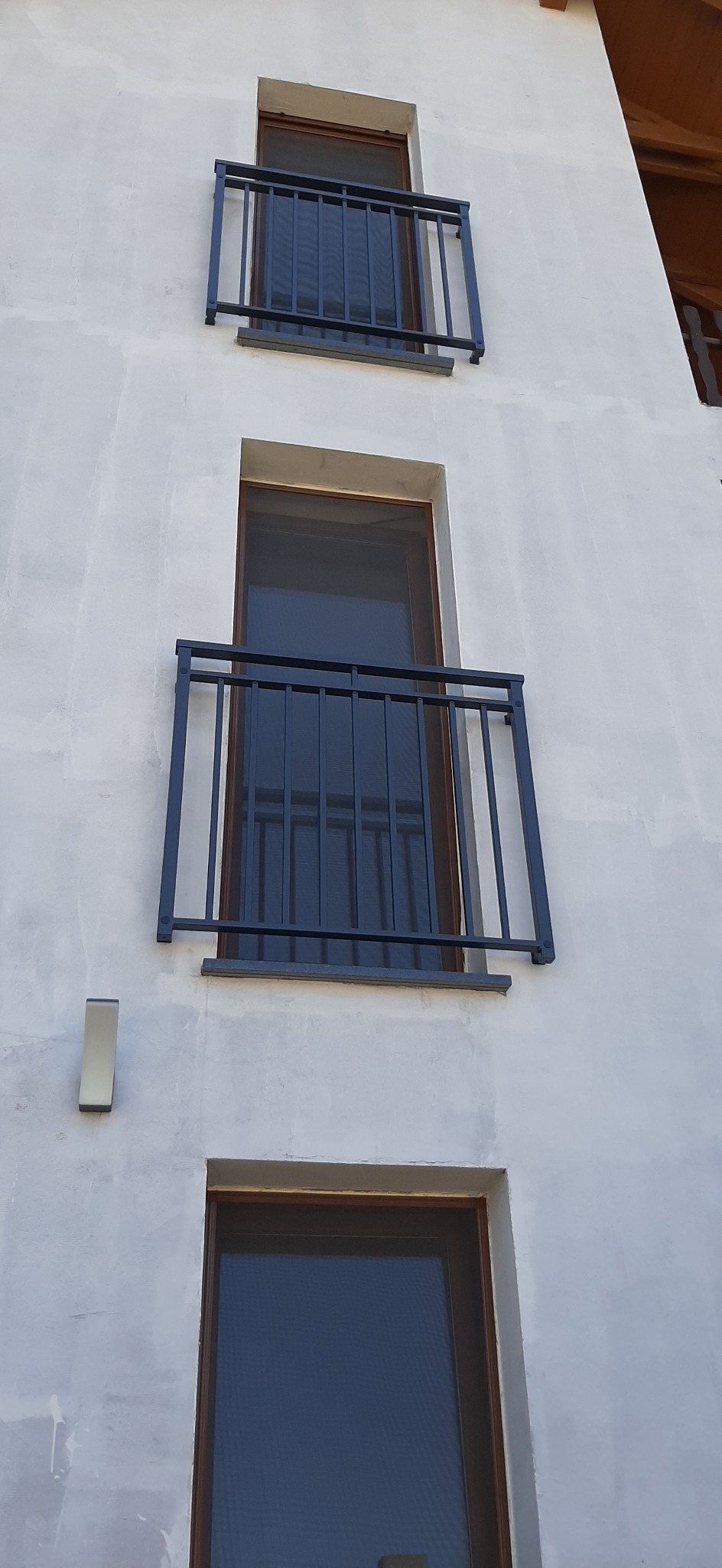 Elewacja budynku z trzema oknami zabezpieczonymi czarnymi, metalowymi balustradami balkonowymi o prostym, nowoczesnym designie.