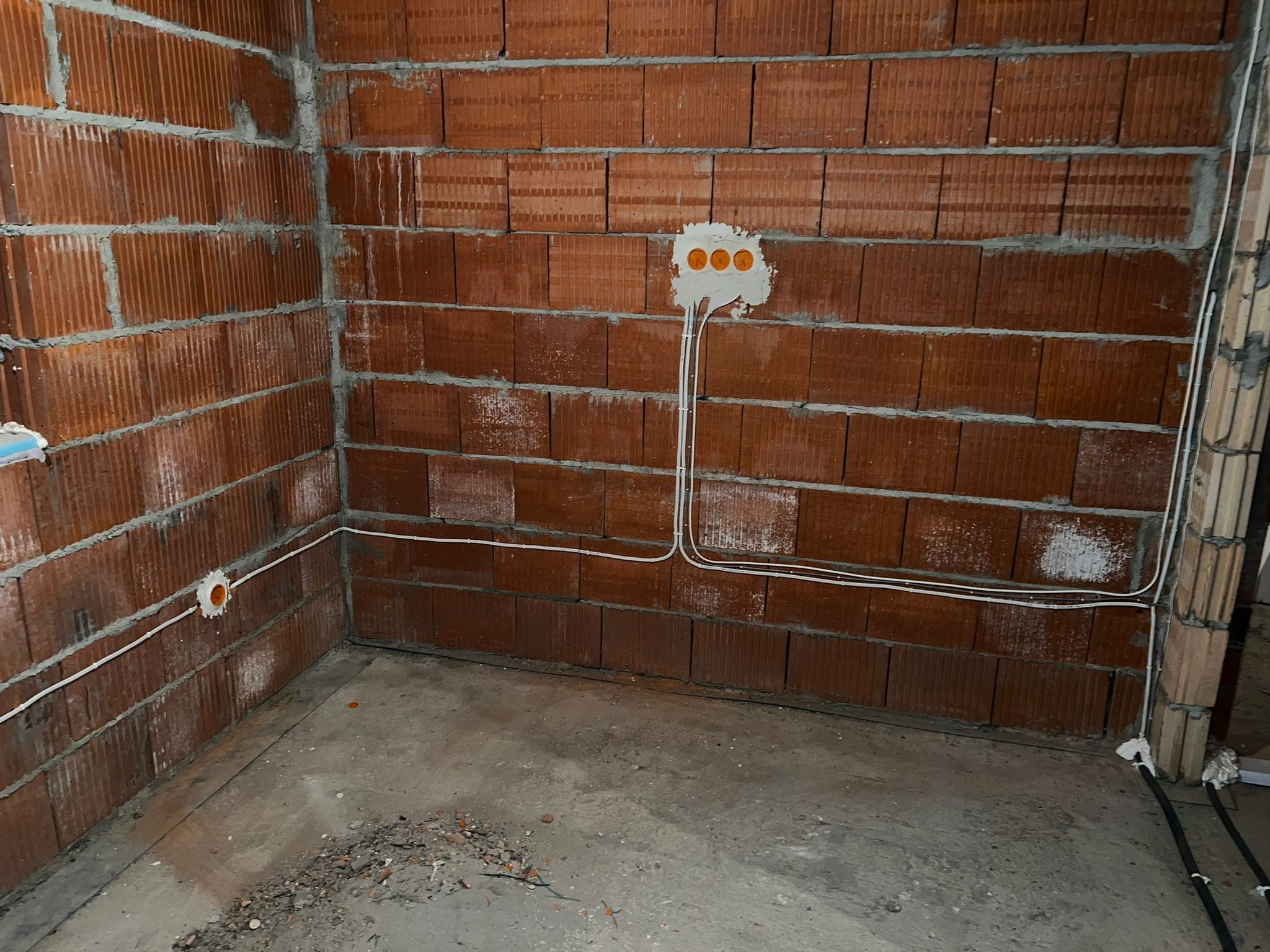 Surowa ściana z cegły ceramicznej z widocznymi puszkami elektrycznymi i przewodami w trakcie montażu instalacji elektrycznej, widoczne ślady zaprawy murarskiej.