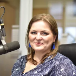 Uśmiechnięta logopedka w niebieskiej bluzce z wzorem, siedząca przed mikrofonem w studio nagraniowym.