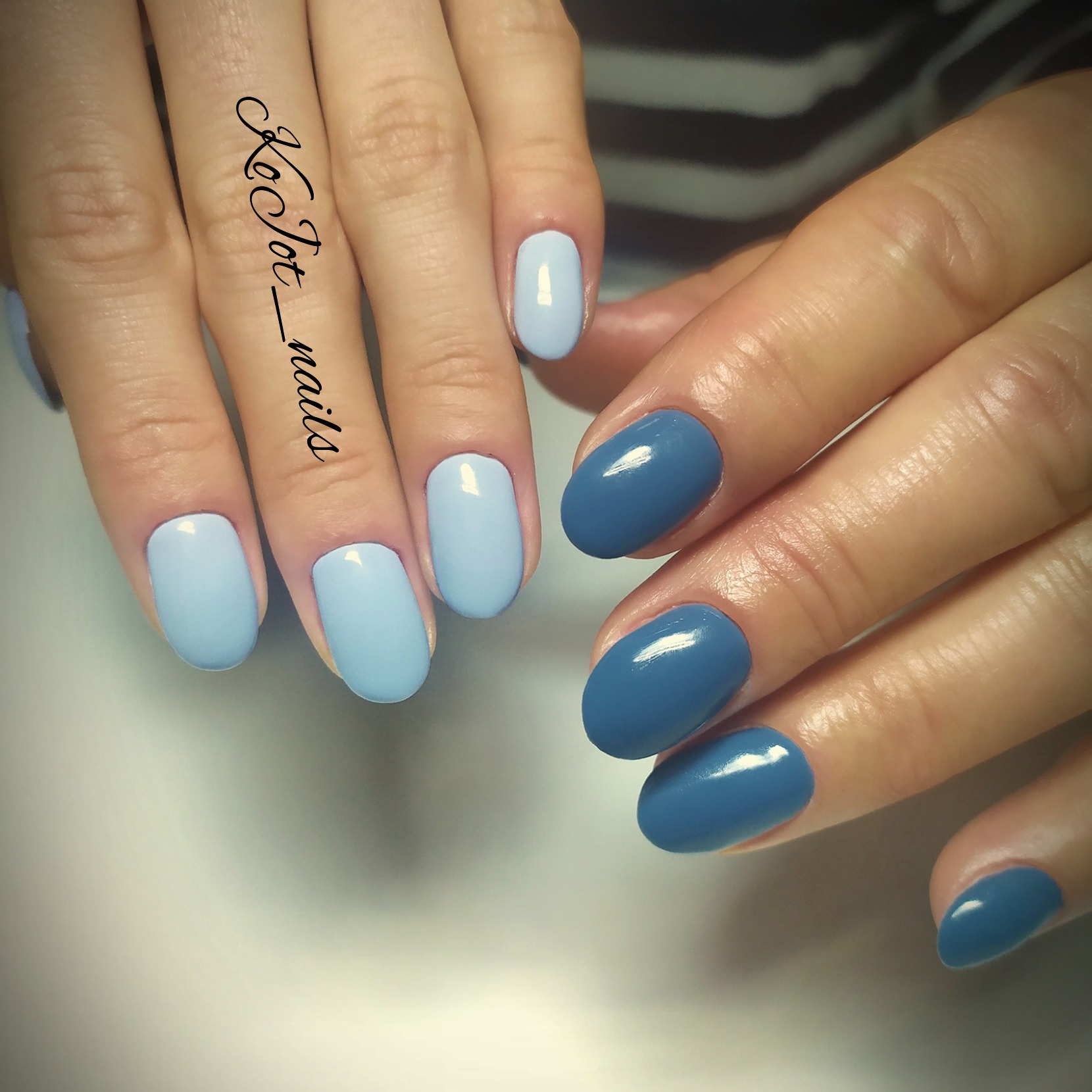 Dłonie z pomalowanymi paznokciami w dwóch odcieniach niebieskiego: jasny pastelowy i ciemniejszy, błyszczący; na palcu napis 'Kot_nails'.