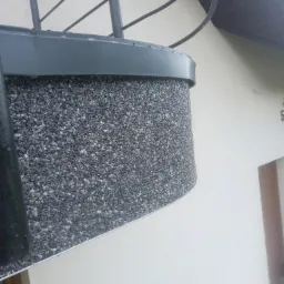 Szary balkon z wykończeniem z drobnych kamyczków, widok z dołu, fragment elewacji budynku w tle.