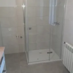 Nowoczesna kabina prysznicowa z przezroczystego szkła, zamontowana w wykafelkowanej łazience w Andrychowie, widoczny grzejnik i odpływ liniowy.