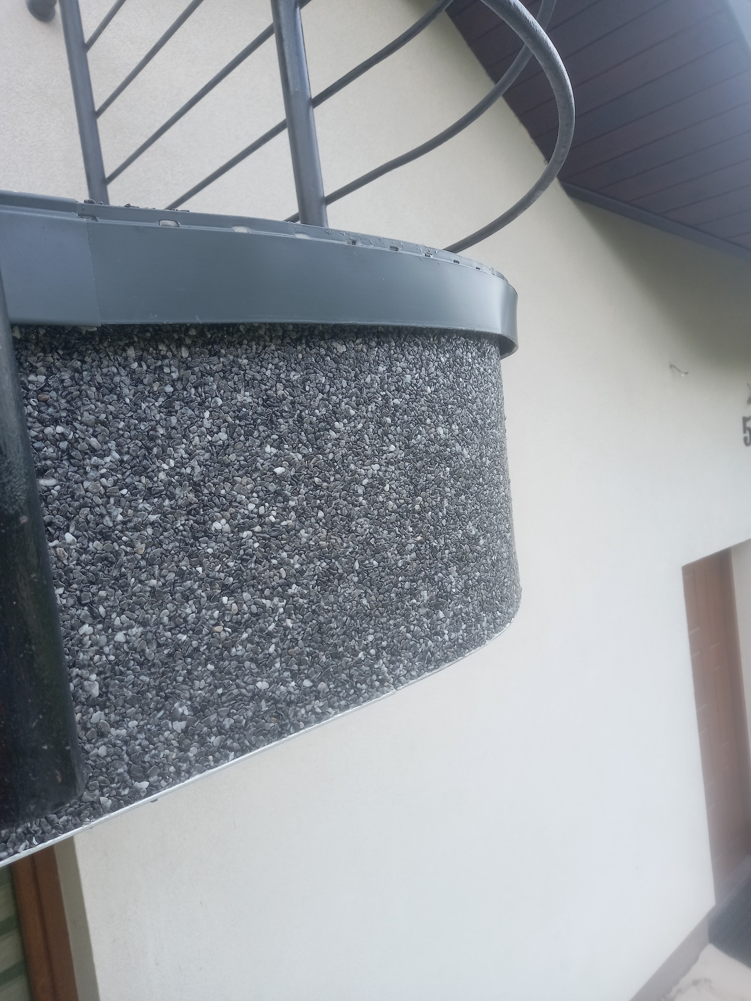 Szary balkon z wykończeniem z drobnych kamyczków, widok z dołu, fragment elewacji budynku w tle.