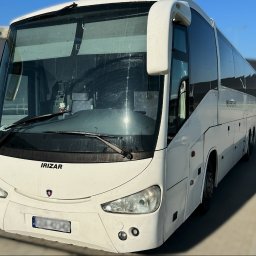 AEROMAX - Biały autokar Irizar na parkingu, widok z przodu, z widoczną maskotką Hello Kitty na desce rozdzielczej oraz osobą w tle.