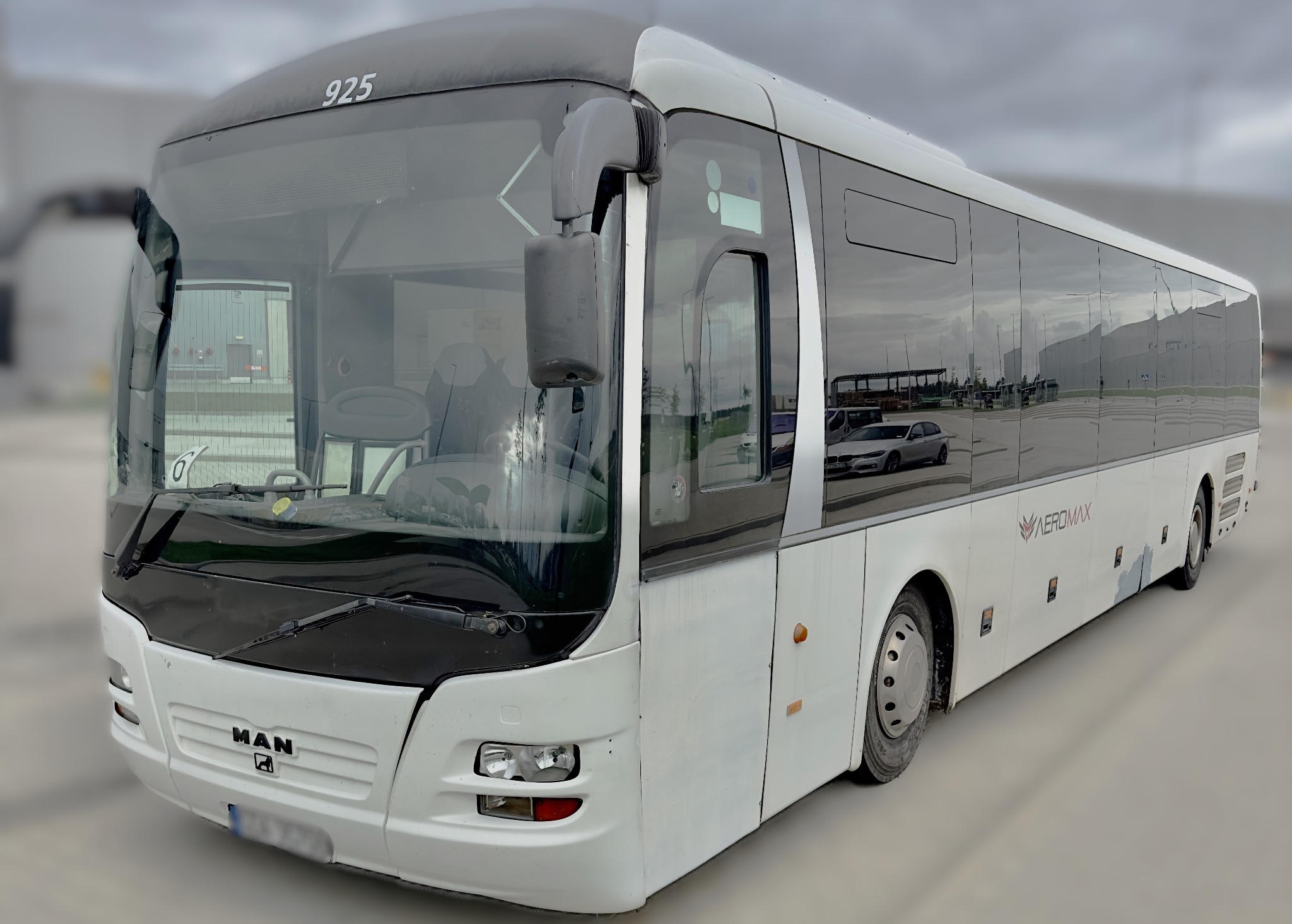 Biały autobus MAN Aeromax z numerem 925 stojący na parkingu, widoczne odbicia budynków i samochodu w szybach.