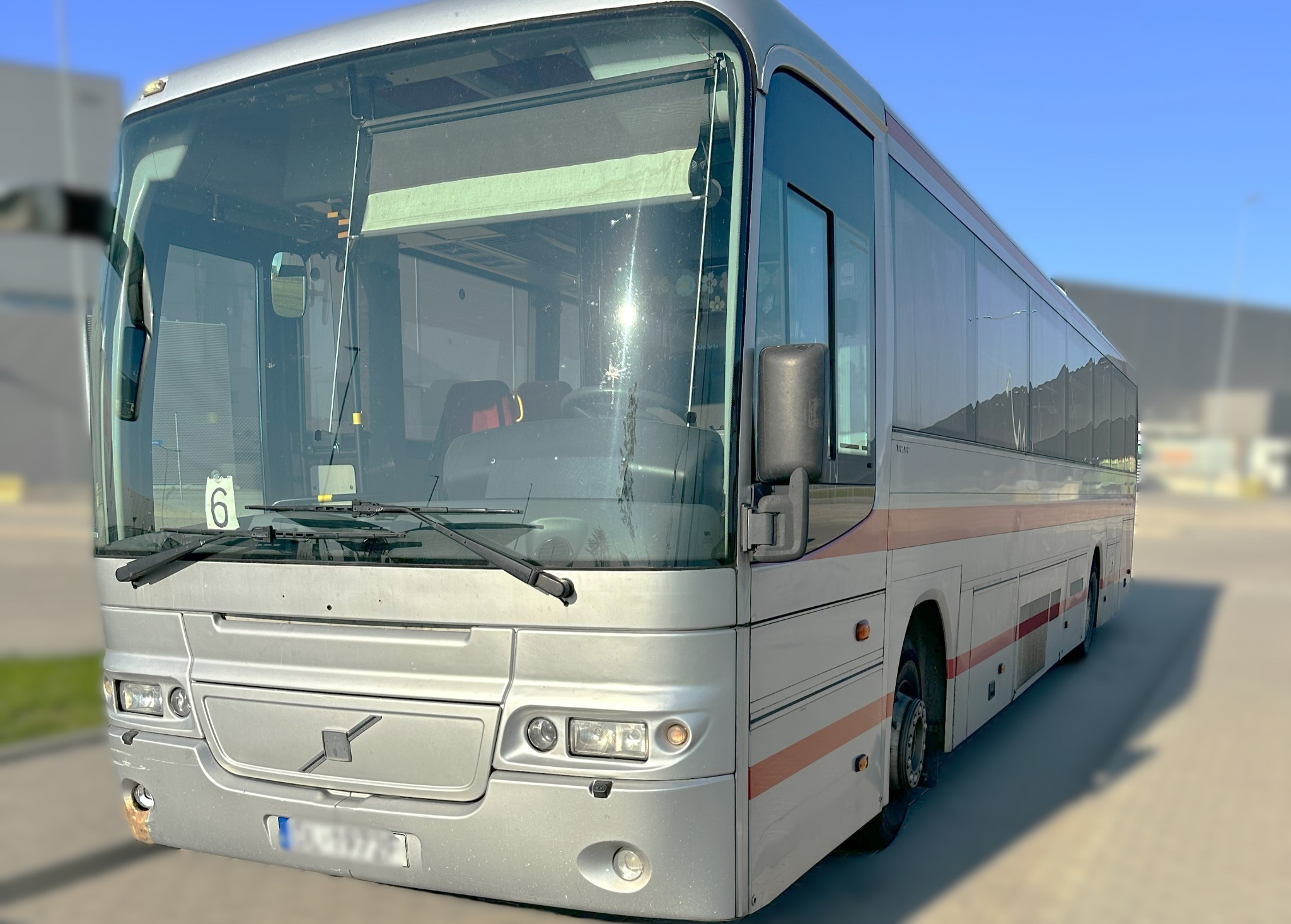 Srebrny autobus Volvo z numerem 6 na przedniej szybie, stojący na parkingu w słoneczny dzień.