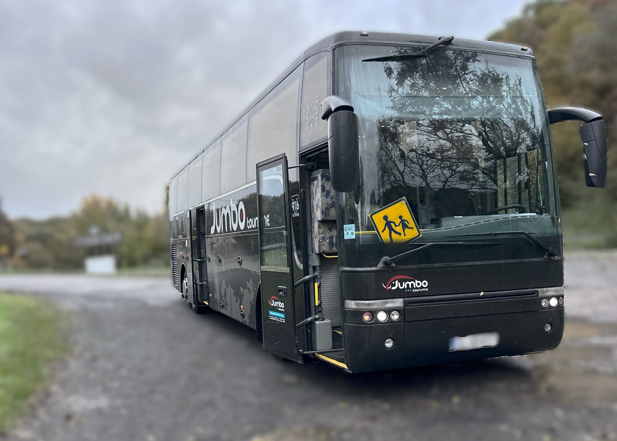 Czarny autokar turystyczny z otwartymi drzwiami, znak ostrzegawczy o przejściu dla dzieci na przedniej szybie, widoczne logo firmy przewozowej na boku i przodzie pojazdu.