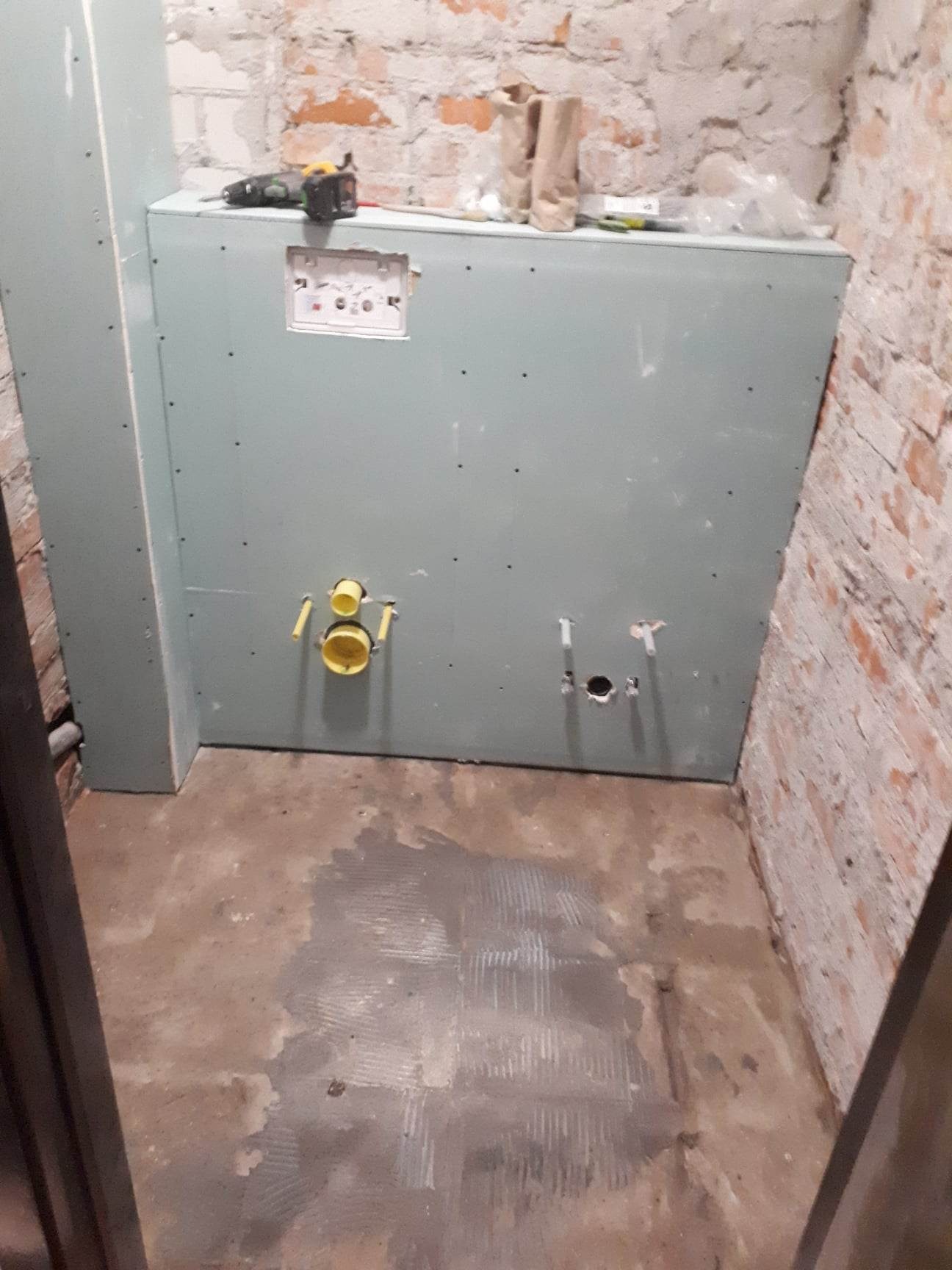 Suche zabudowy w toalecie w trakcie remontu, widoczne podejścia hydrauliczne do bidetu i Geberitu, ściany z surowej cegły, narzędzia na obudowie.