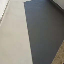 Szara, gładka powierzchnia balkonu po hydroizolacji w Mikołowie, widoczne ślady po wałku malarskim i cień barierki.