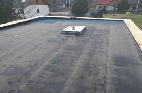 Płaski dach pokryty papą z zamontowanym świetlikiem dachowym, widok z góry, w tle zabudowa jednorodzinna.