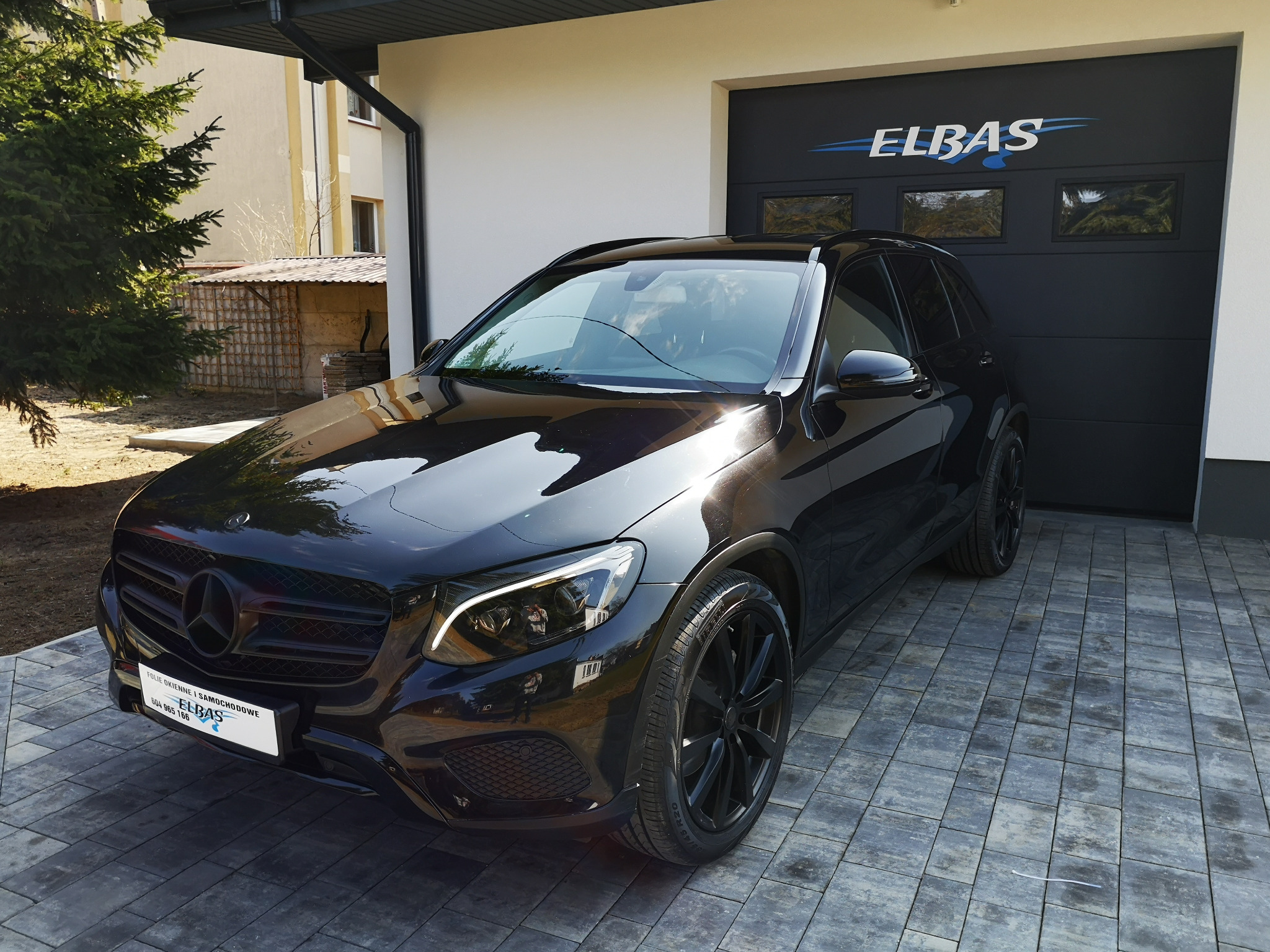 Czarny SUV Mercedes-Benz z przyciemnionymi szybami i czarnymi felgami zaparkowany przed garażem z logo firmy Elbas.