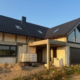 Kierownik Budowy/Inspektor Nadzoru Krystian Lindstaedt - Dom jednorodzinny w trakcie budowy, widoczne białe bloczki konstrukcyjne, czarny dach z dachówki, duże okna z czarnymi ramami i niezabudowany teren wokół.