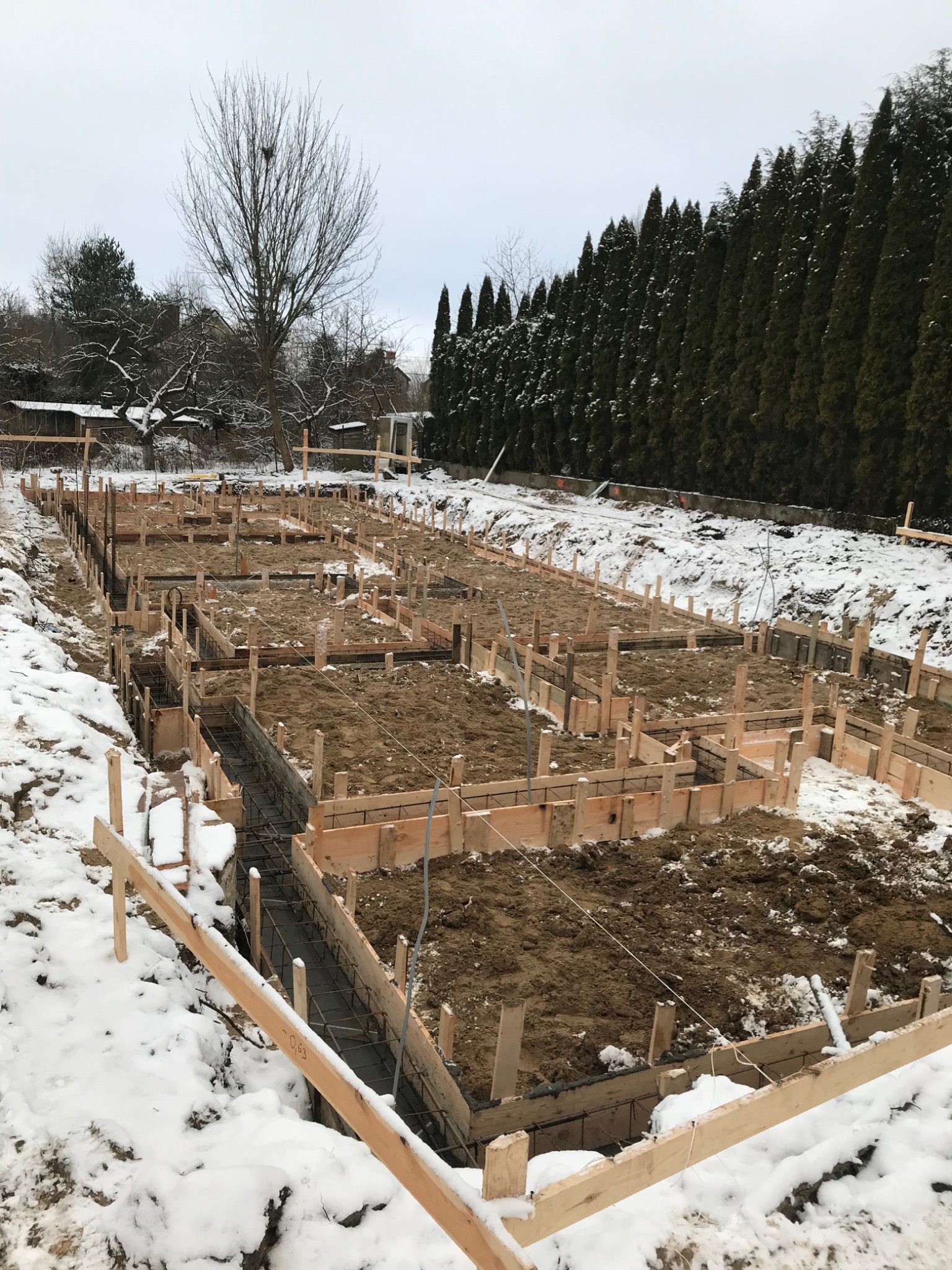 Przygotowanie fundamentów pod budynek jednorodzinny w zimowej scenerii, widoczne deskowanie i zbrojenie.